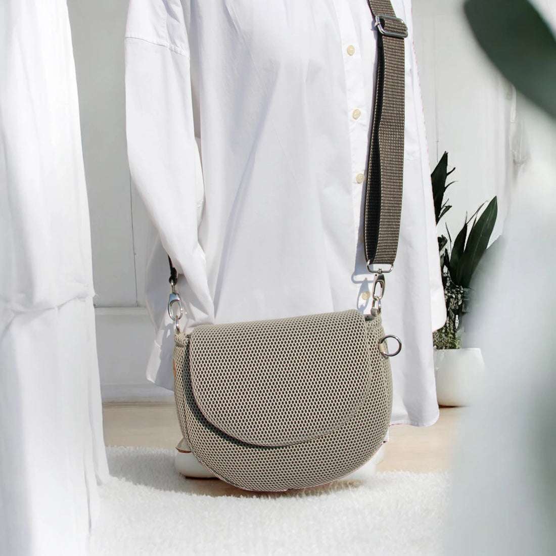 Halbrunde medium sized Gassitasche in Farbe beige aus Mesh Material mit beige_schwarzem Tragegurt über Puppe hängend der Hintergrund ist minimalistisch