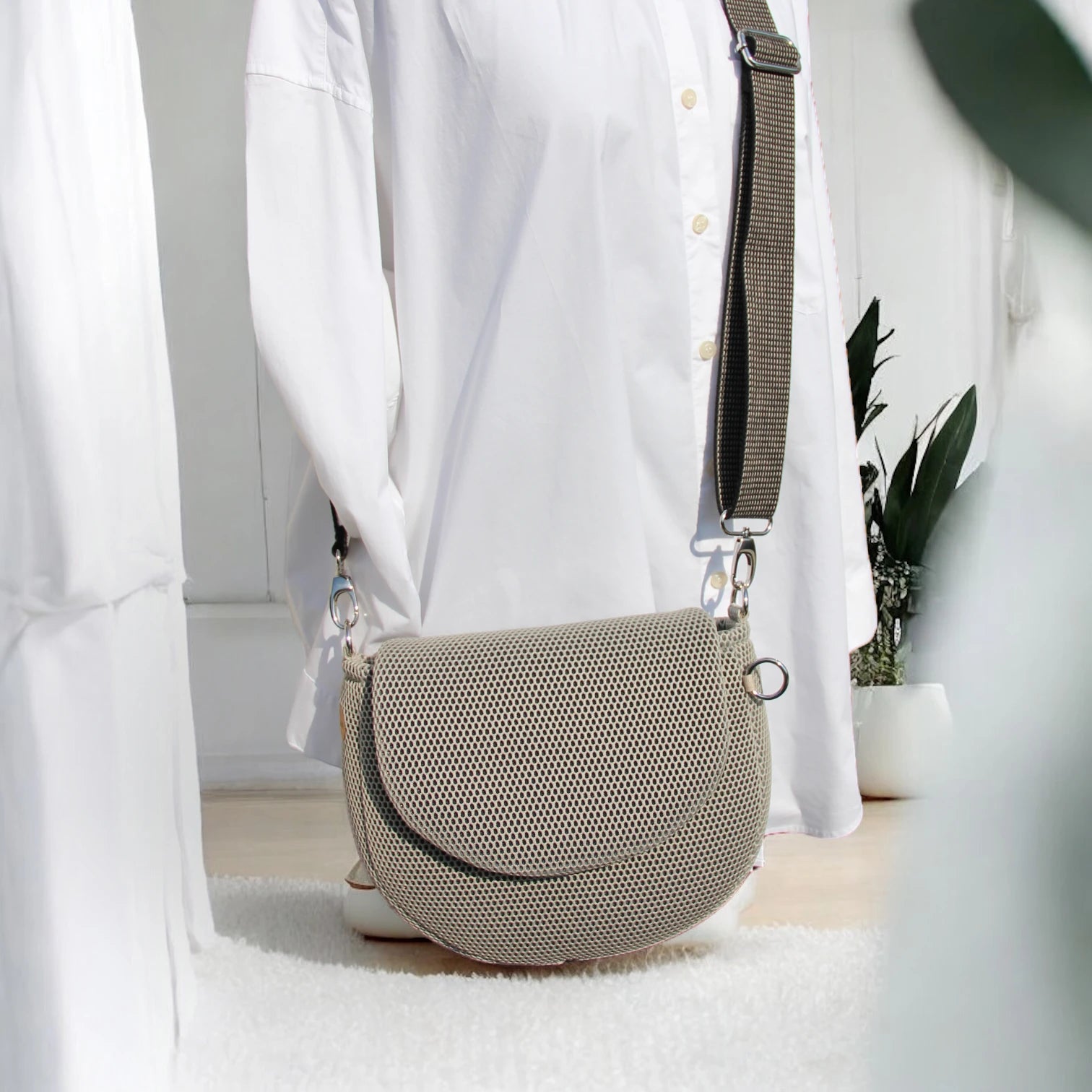 Halbrunde medium sized Gassitasche in Farbe beige aus Mesh Material mit beige_schwarzem Tragegurt über Puppe hängend der Hintergrund ist minimalistisch