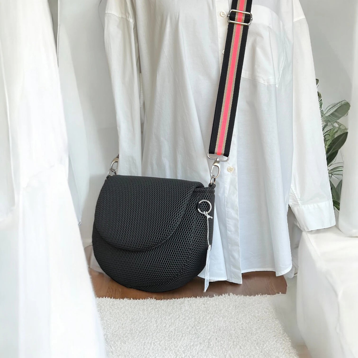 Halbrunde medium sized Gassitasche in Farbe schwarz aus Mesh Material mit schwarz__koralle farbenen Tragegurt über Puppe hängend der Hintergrund ist minimalistisch