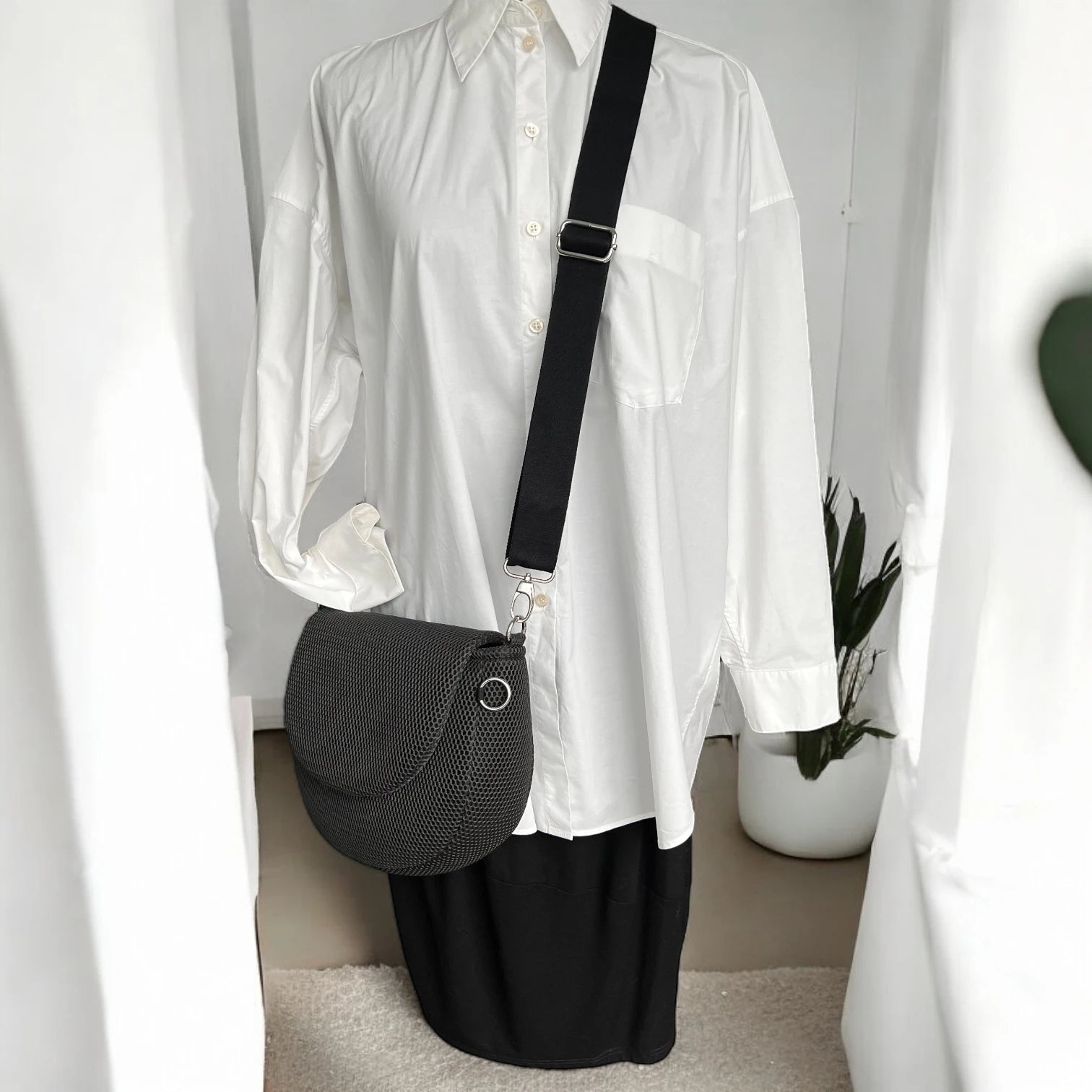 Halbrunde medium sized Gassitasche in Farbe schwarz aus Mesh Material mit schwarzen Tragegurt über Puppe hängend der Hintergrund ist minimalistisch