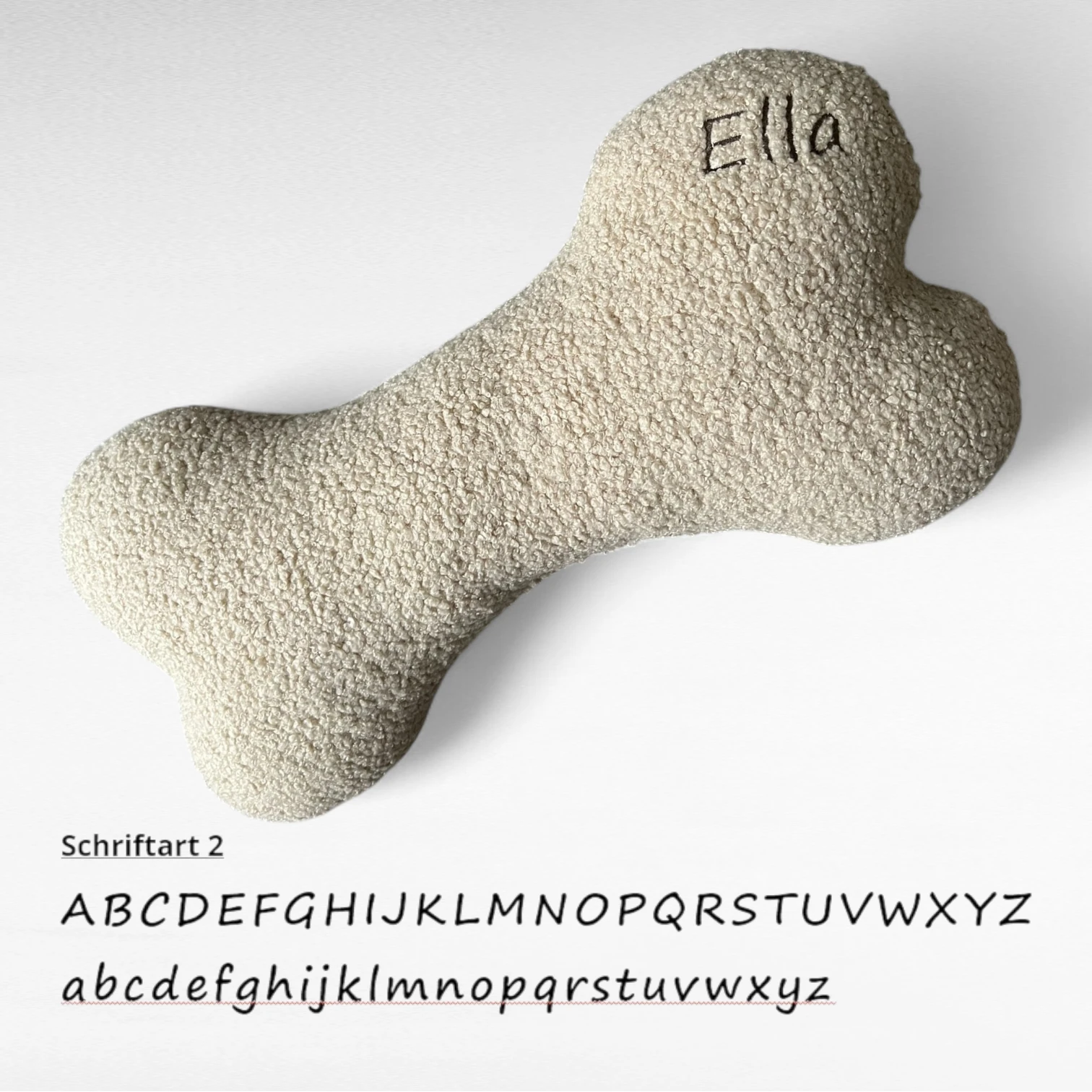 Kuscheliges Hundekissen in Knochenform aus Bouclestoff in beige mit brauner Namensstickerei Ella als Beispiel in Schriftart 2