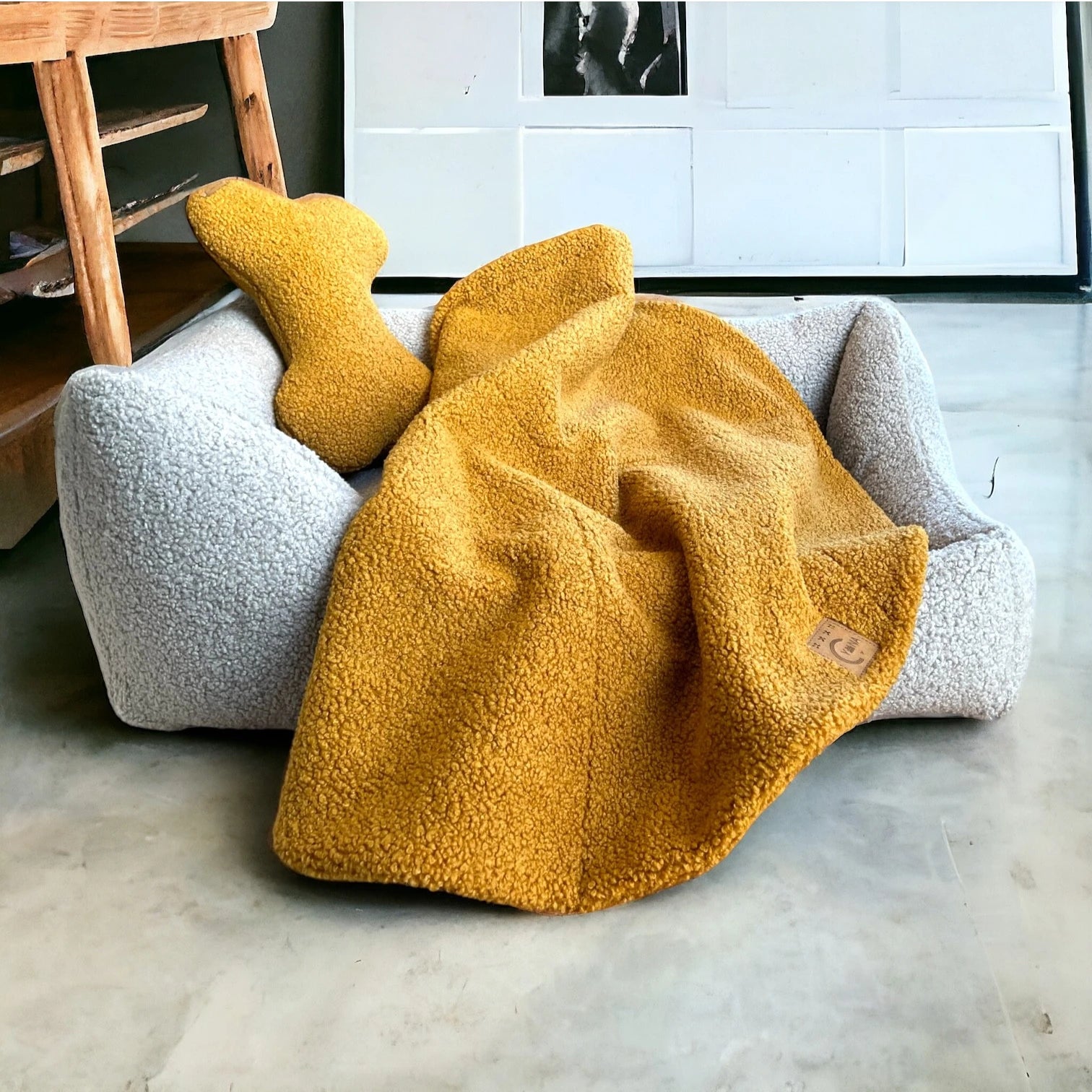 Safranfarbene rechteckige Hundedecke mit abgerundeten Ecke und Ziersteppungen aus hochwertigem Boucle-Stoff und Hundekissen in Knochenform über Hundebett mit Bouclebezug hellgrau mit asymmetrischen Seitenpolstern in minimalistischem Raum