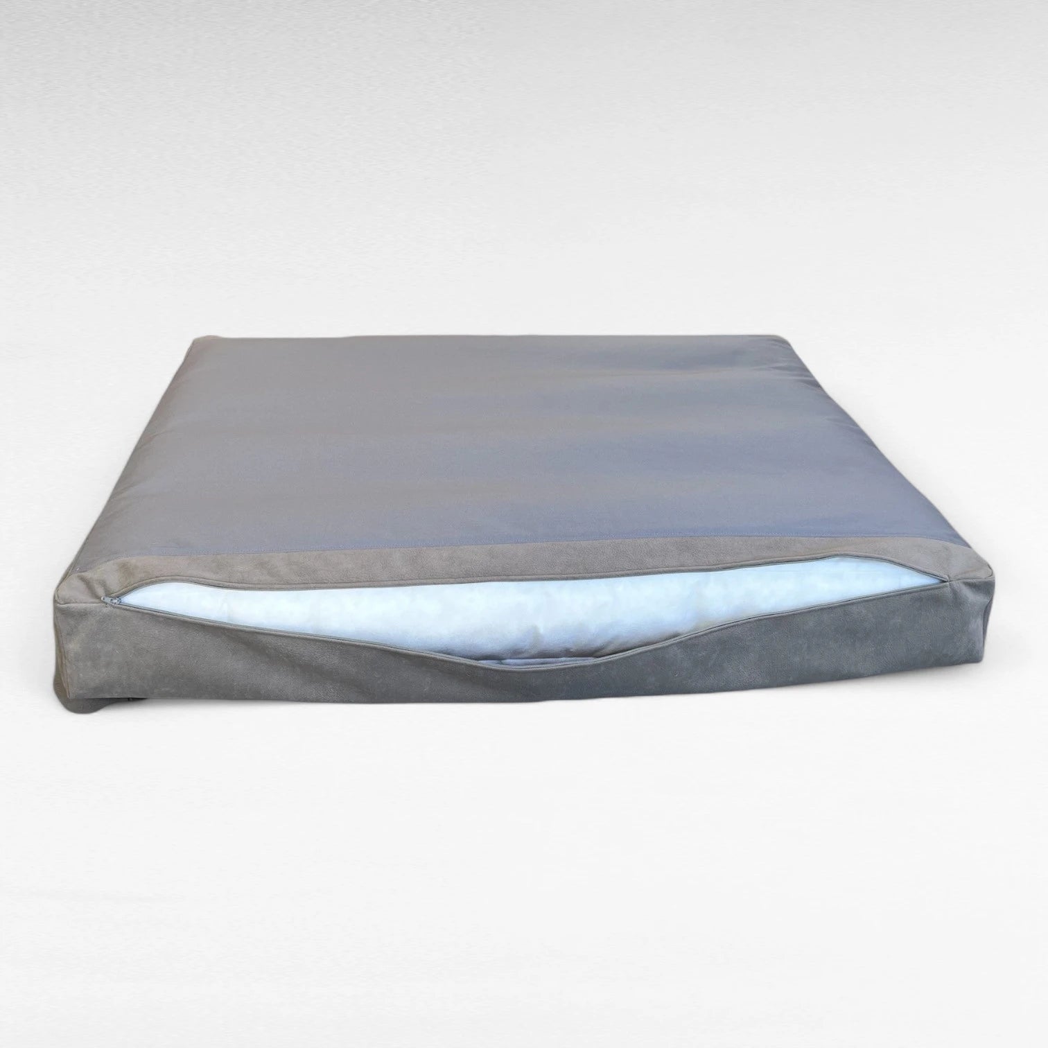 Rechteckiges Hundebett mit geöffnetem Reißverschluß auf dem Kopf liegend, weiße Matratze schaut heraus