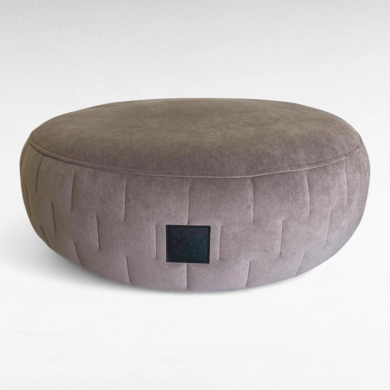 Rundes othopädisches Hundebett Yuna taupe mit seitlichen Steppungen und schwarzem Yuna Label. Der Stoff ist ein Velours Stoff