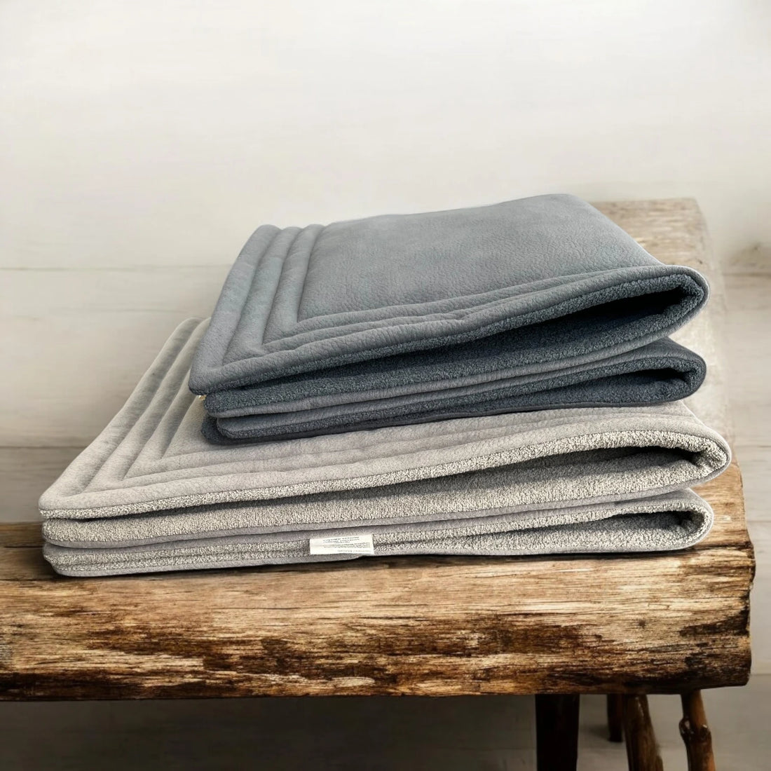 2 gefaltete In und Outdoorhundedecken in anthrazit oben und schlamm unten im Stapel auf einem Holztisch liegend