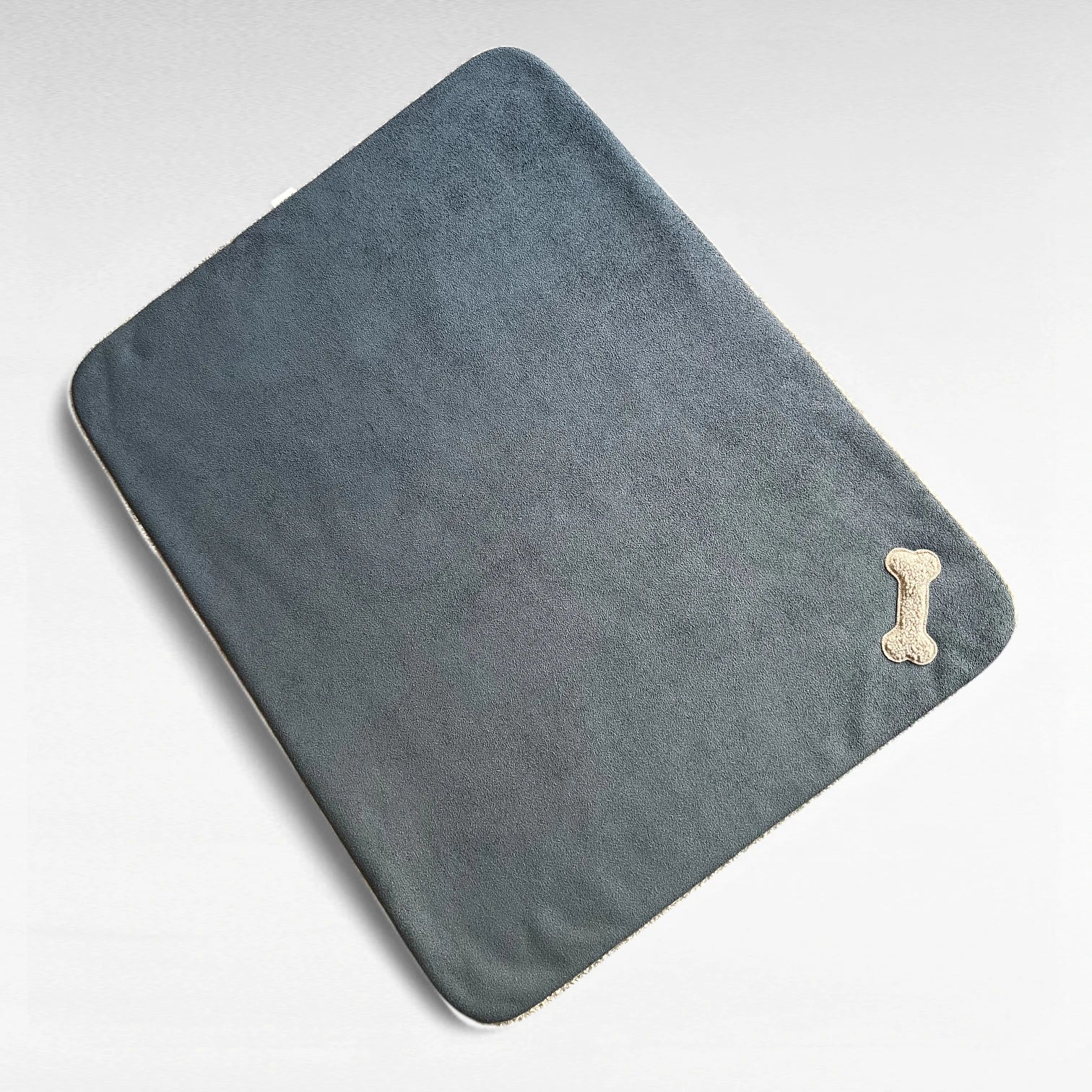 Rechteckige Hundedecke in Farbe anthrazit mit knochenförmiger Teddyapplikation in Farbe taupe in der Ecke und rundlaufendem Paspel in Farbe taupe