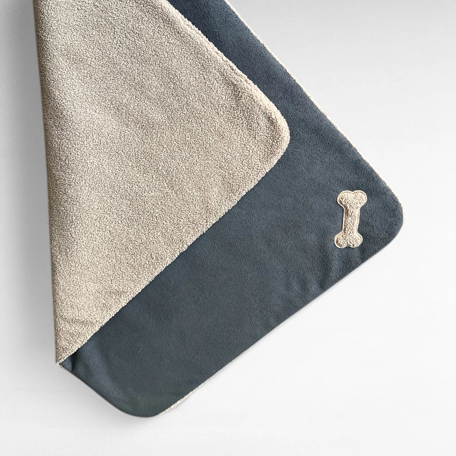 Rechteckige Hundedecke anthrazit_taupe halb gefaltet mit beidseitig sichtbarem Material mit knochenförmiger Applikation aus Teddystoff in taupe