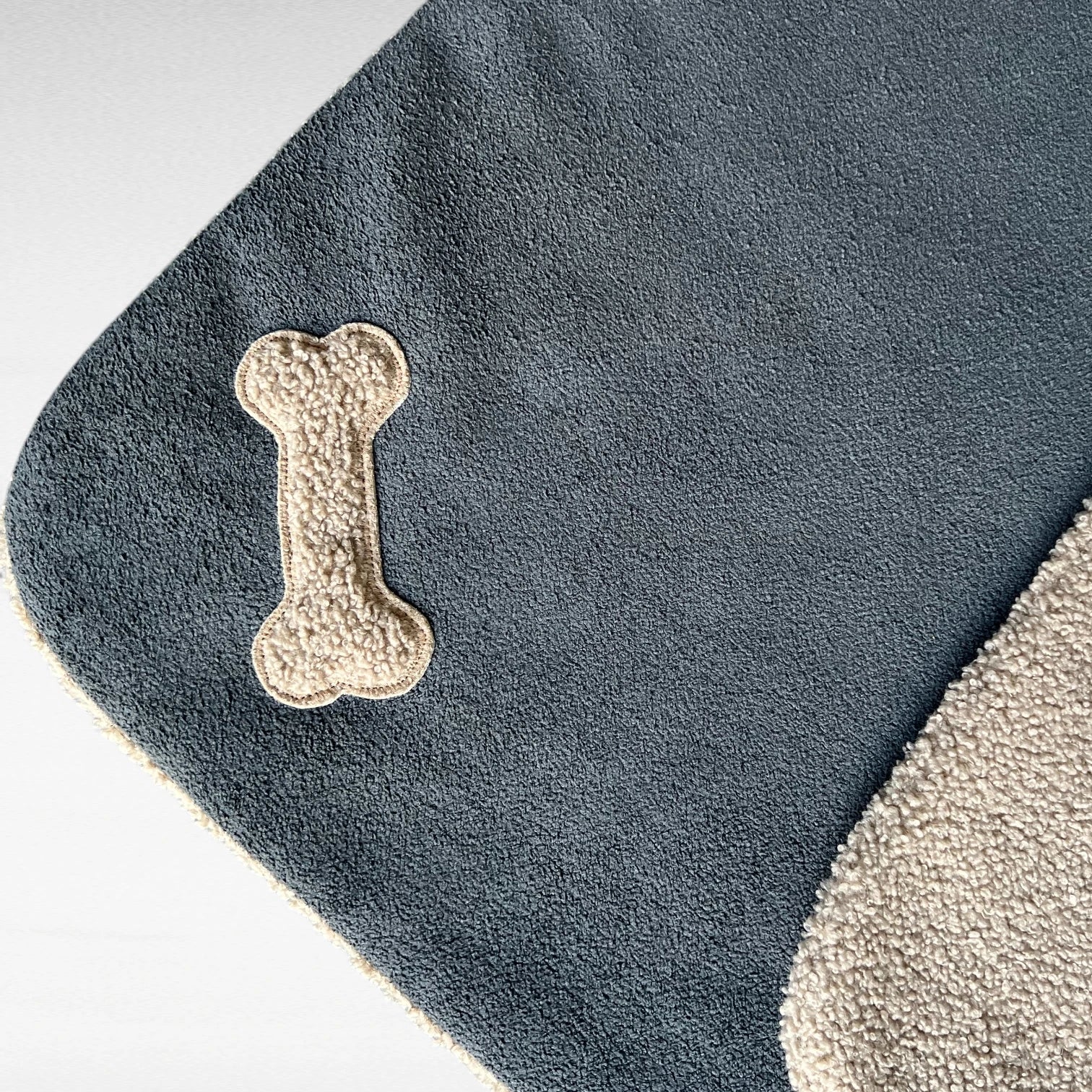 Detailansicht knochenförmige Teddyapplikation in Ecke auf Hundedecke in Farbe taupe