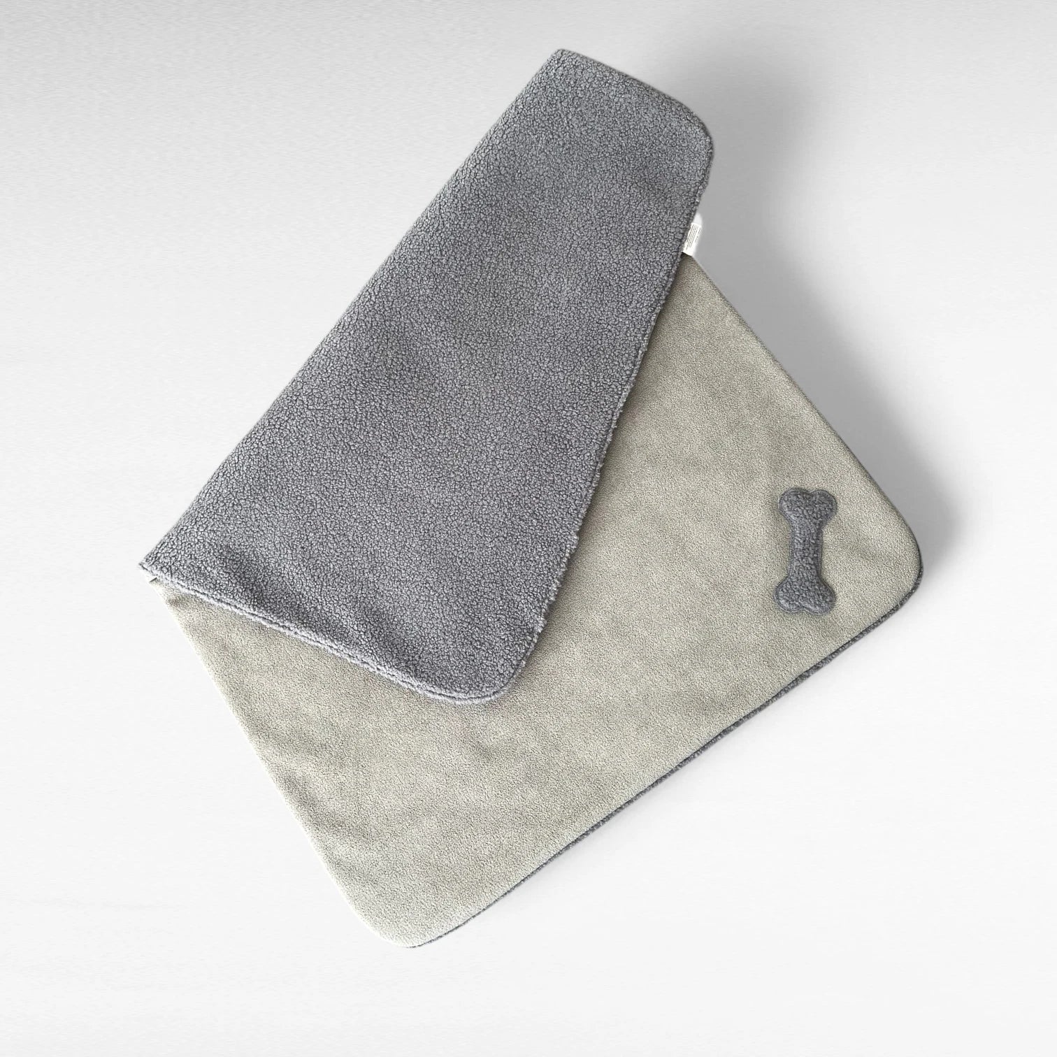 Rechteckige Hundedecke schlamm_grau halb gefaltet mit beidseitig sichtbarem Material mit knochenförmiger Applikation aus Teddystoff in grau