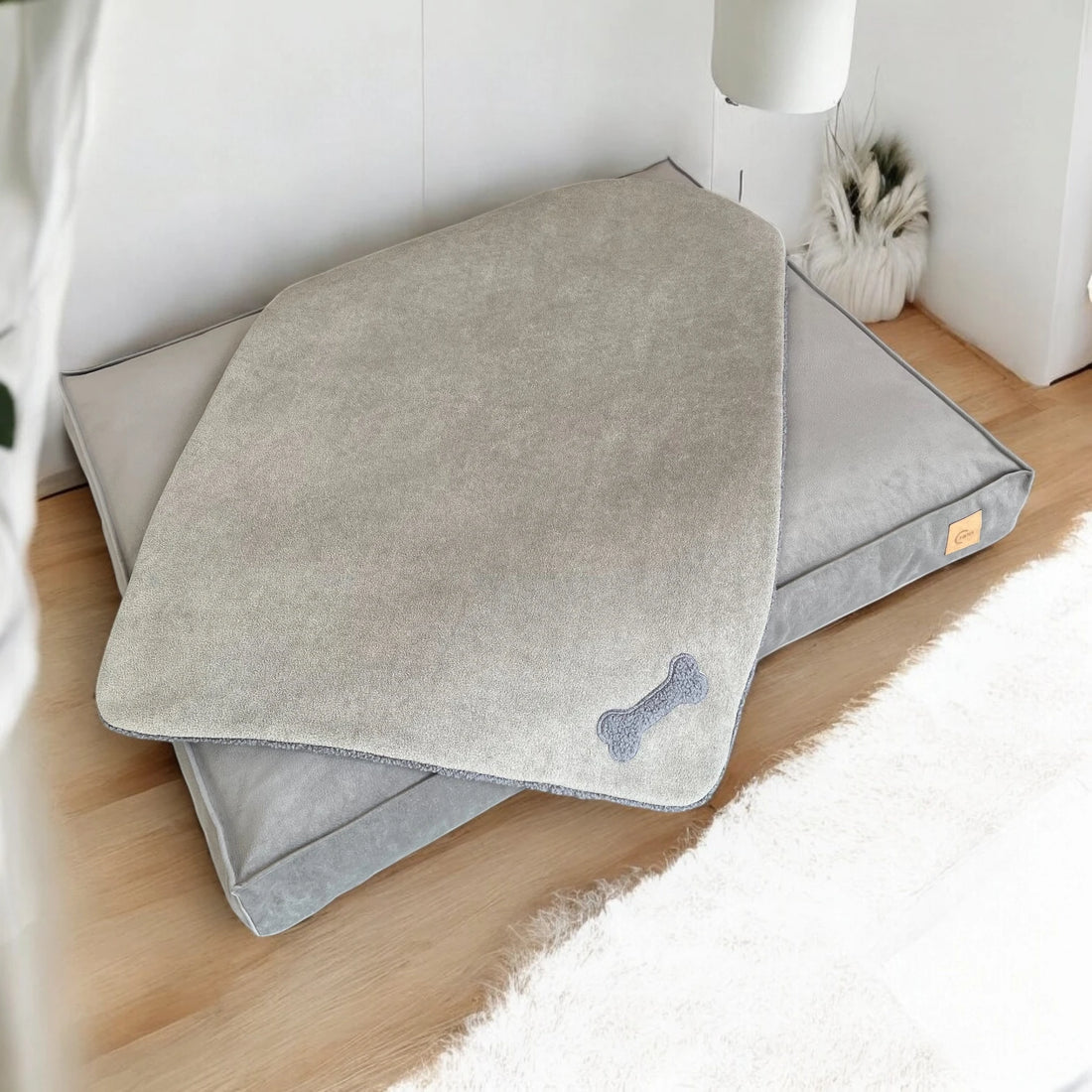 Rechteckige Hundedecke in Farbe schlamm mit grauer Applikation aus Teddystoff in Knochenform über rechteckigem Hundebett in Farbe greige liegend