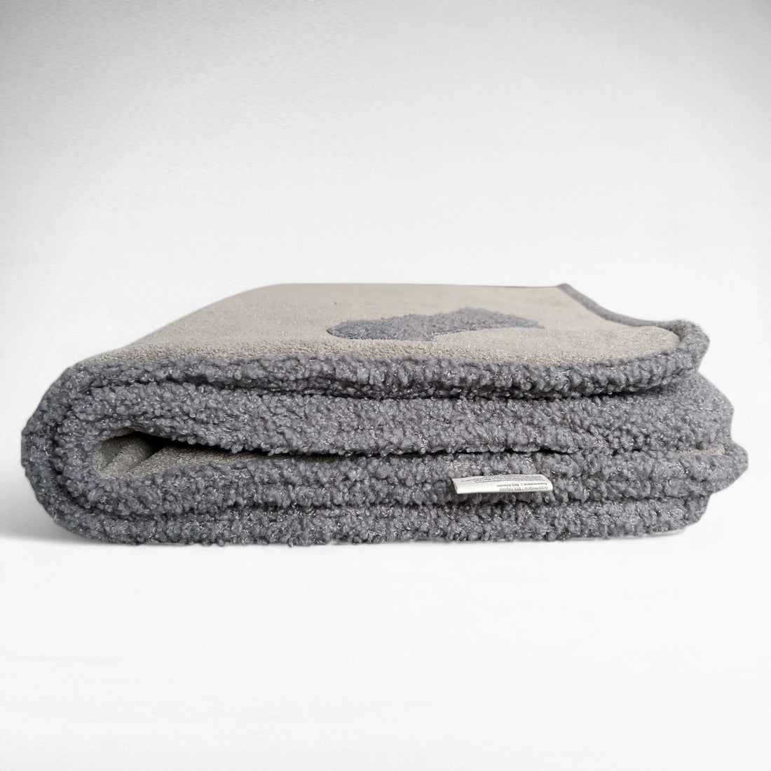 Frontalansicht vierfach gefaltete Decke aus grauem Teddystoff und schlammfarbenen Stoff auf der Oberseite und grauem Paspel aus Teddystoff