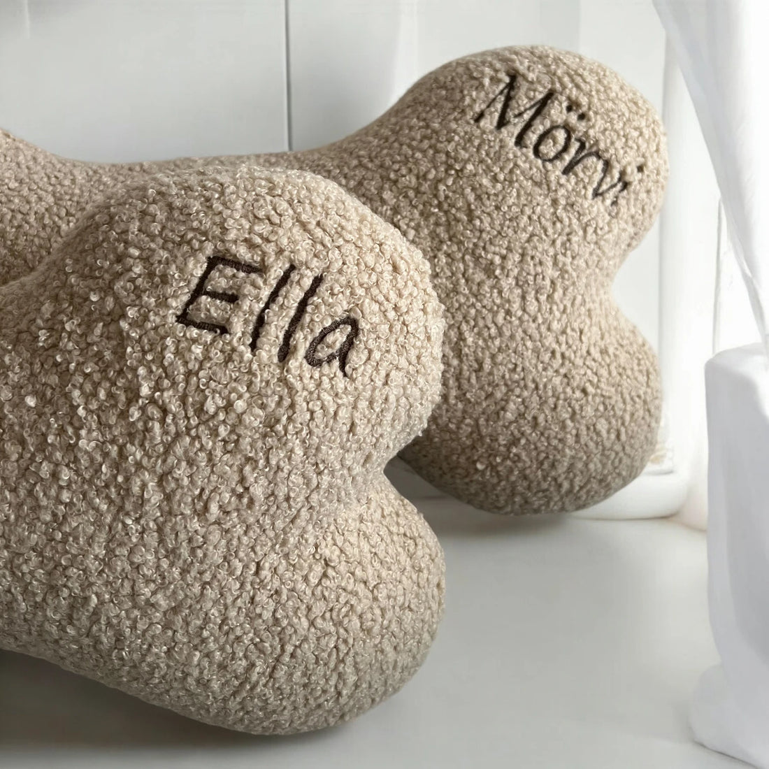 2 halbe Hundekissen in Knochenform aus beigen Teddystoff mit Namenstickerei in Farbe braun