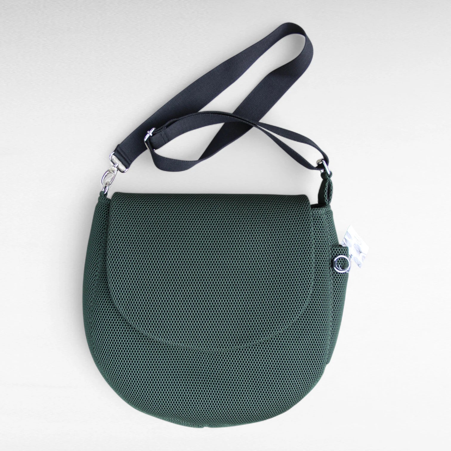 Runde oversized -Tasche mit Taschenklappe aus dunkelgrünem Mesh Material mit schwarzem Gurt und Metallelemente in silber