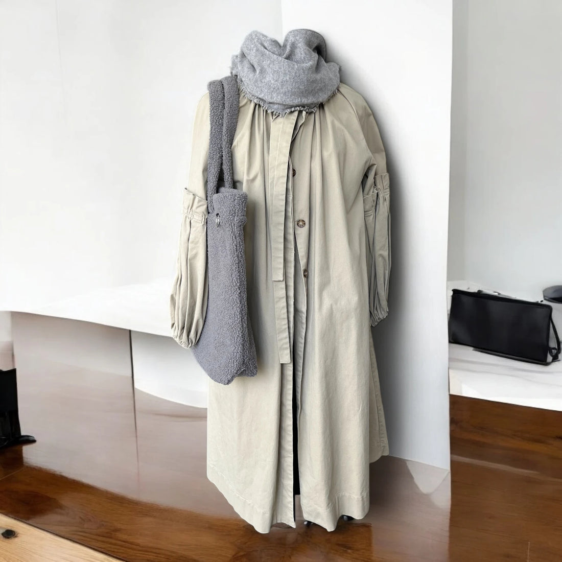 Frontansicht grauer Shopper aus Teddyfell über Puppe hängend mit beigem Mantel und grauem Wollschal mit minimalistischem Raumhintergrund