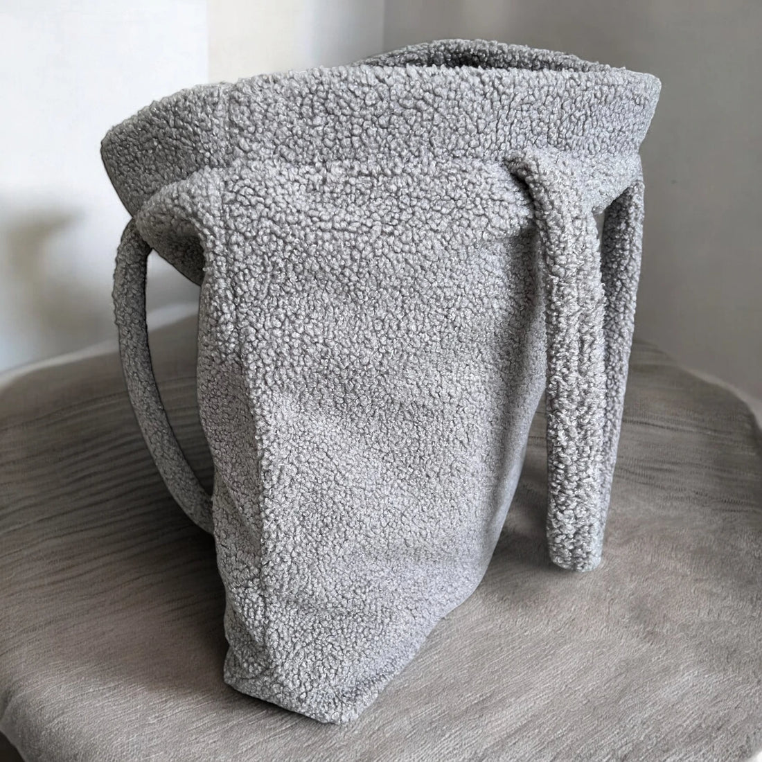 Rechteckiger Shopper aus Teddyfell in Farbe grau stehend und halb geöffnet mit minimalistischem Hintergrund
