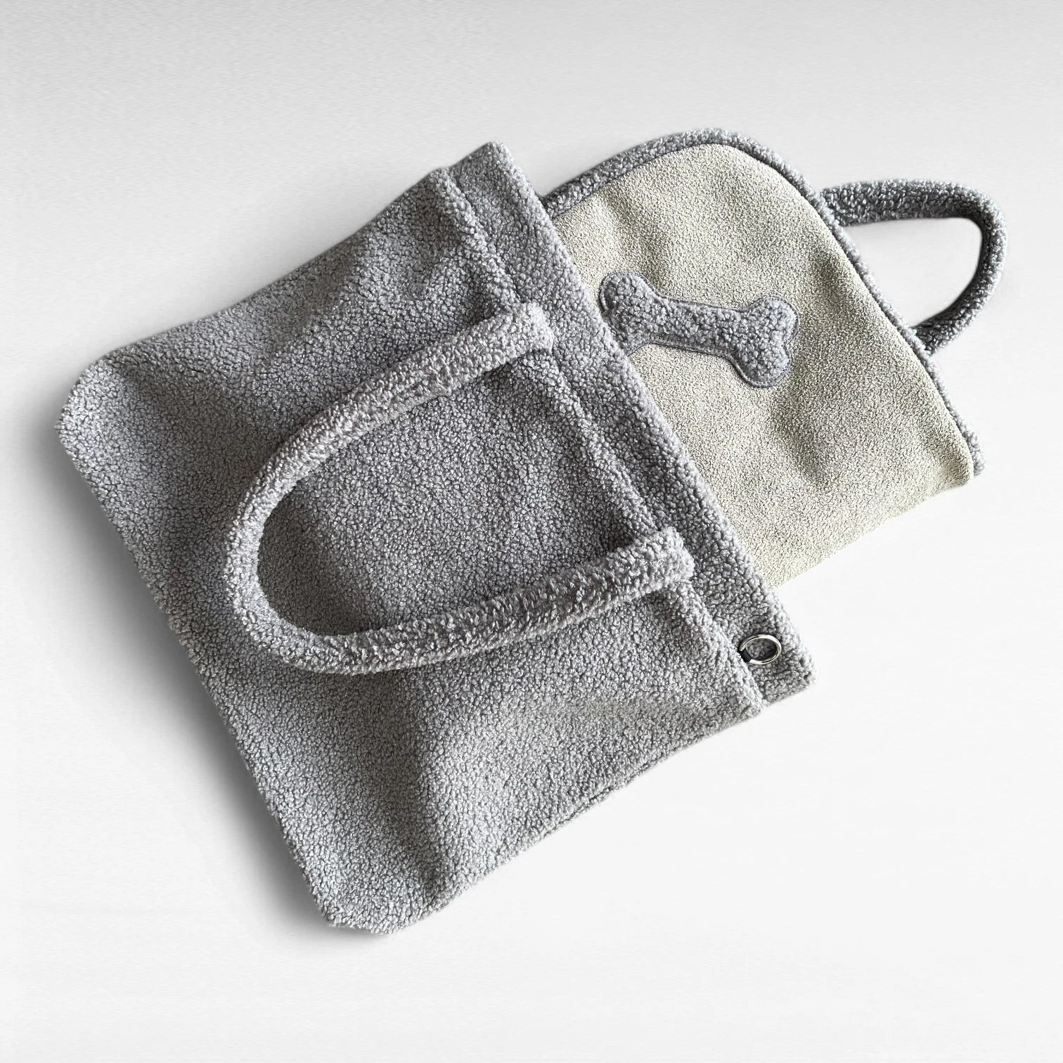Grauer rechteckiger Teddyfellshopper mit schlammfarbener Hundedecke mit Knochenapplikation halb herausschauend