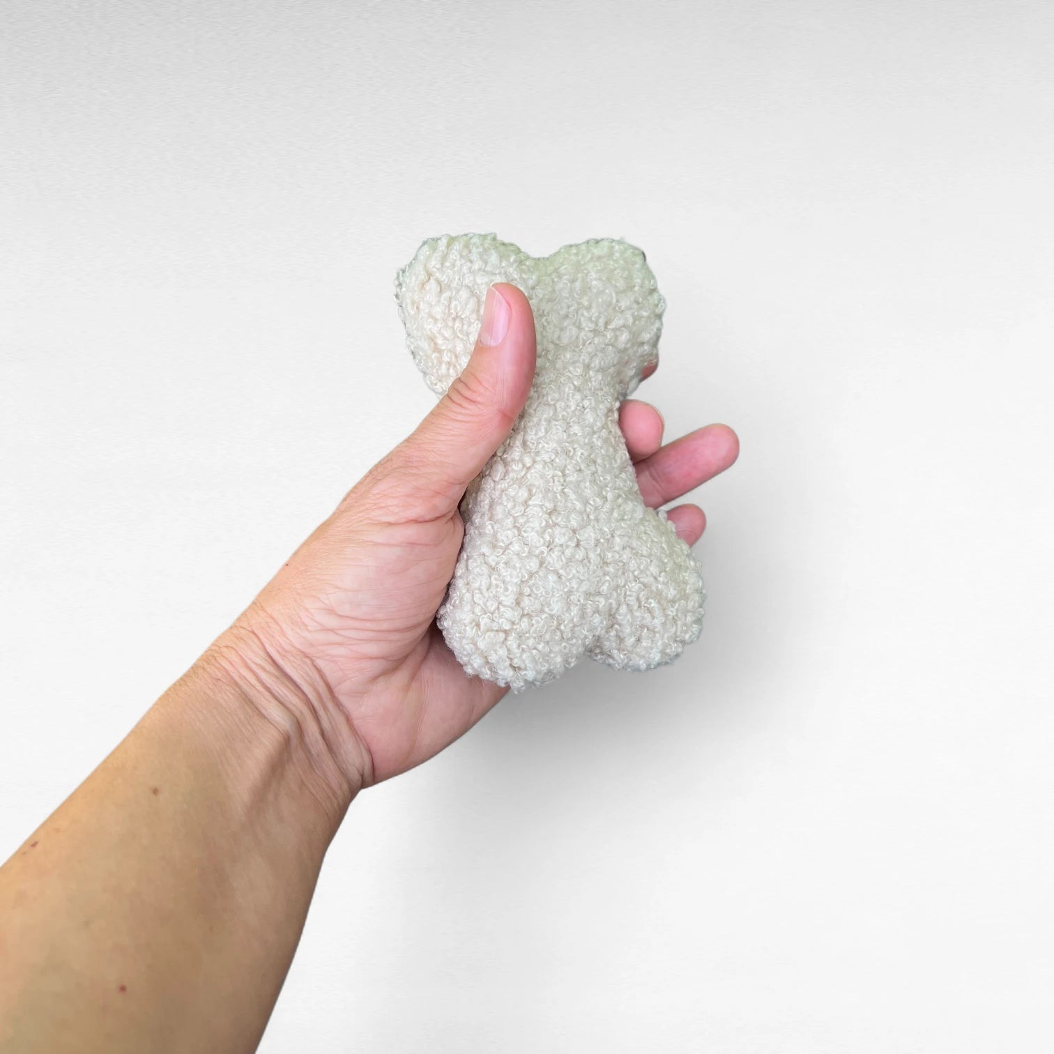 Beiger Taschenanhänger aus Boucle in Knochenform in Hand zum Größenvergleich liegend