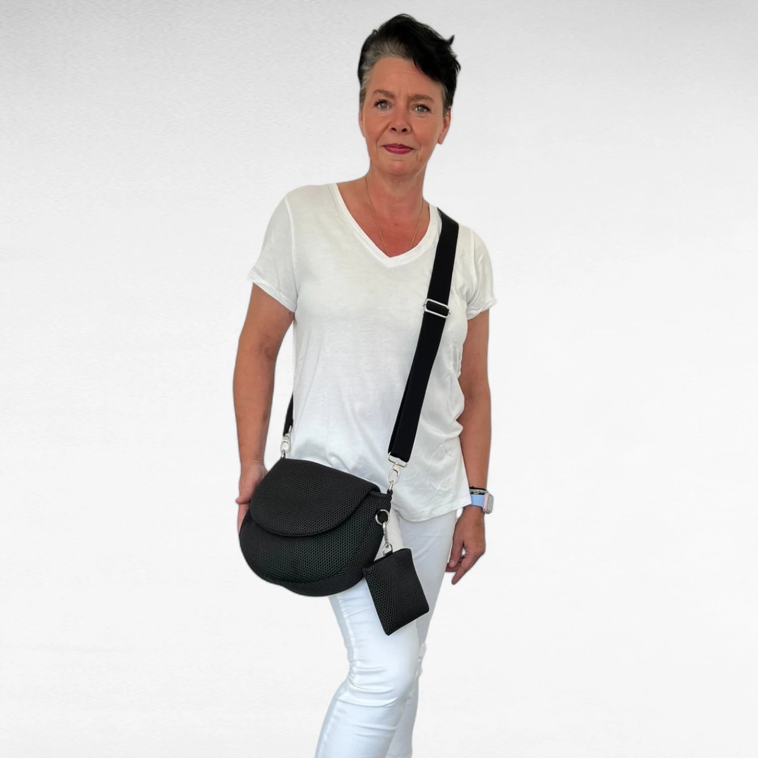 Frau in weiß gekleidet trägt halbrunde Gassitasche aus Mesh Material in schwarz mit schwarzem Tragegurt und Leckerlibeutel schwarz