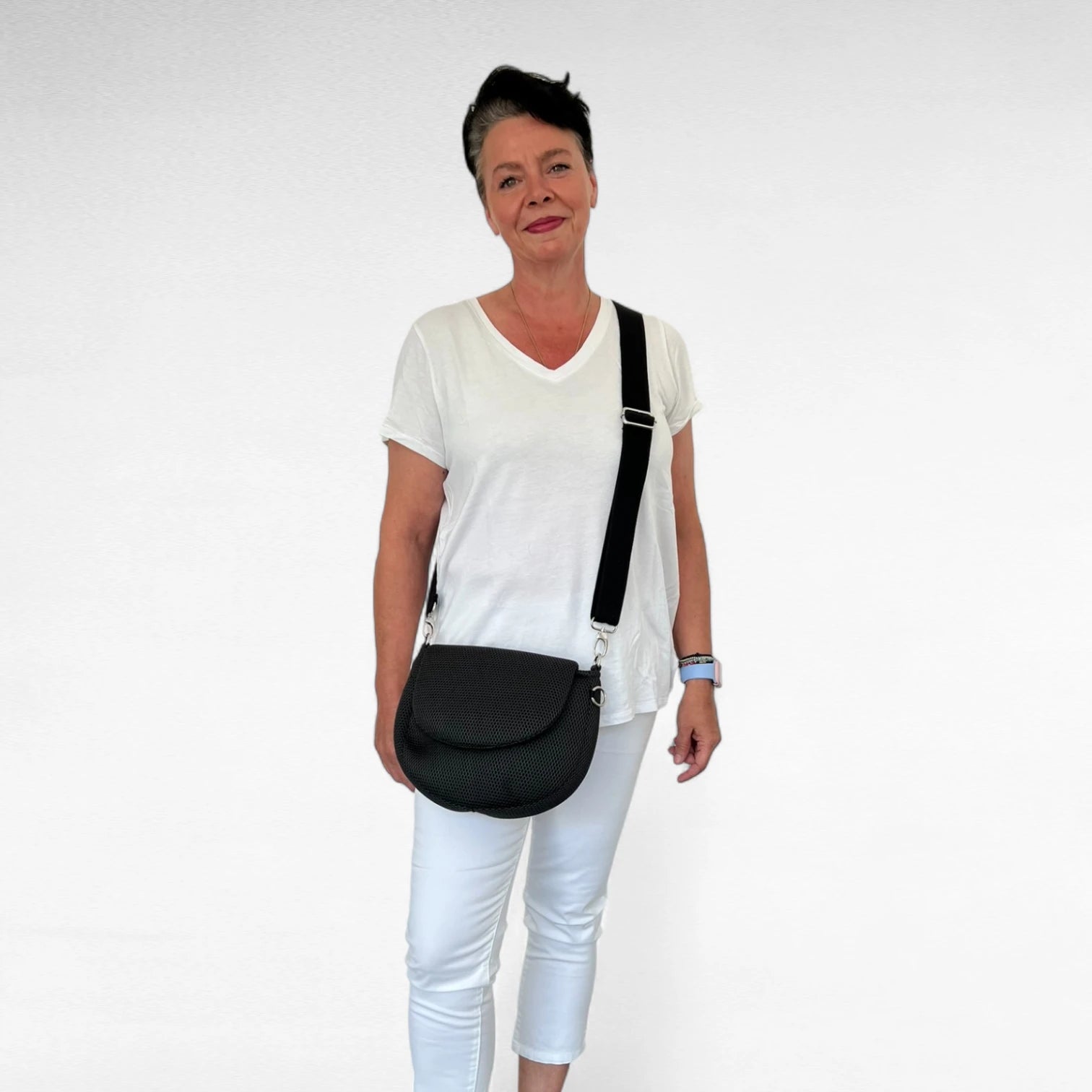 Frau in weiß gekleidet trägt halbrunde Gassitasche aus Mesh Material in schwarz mit schwarzem Tragegurt