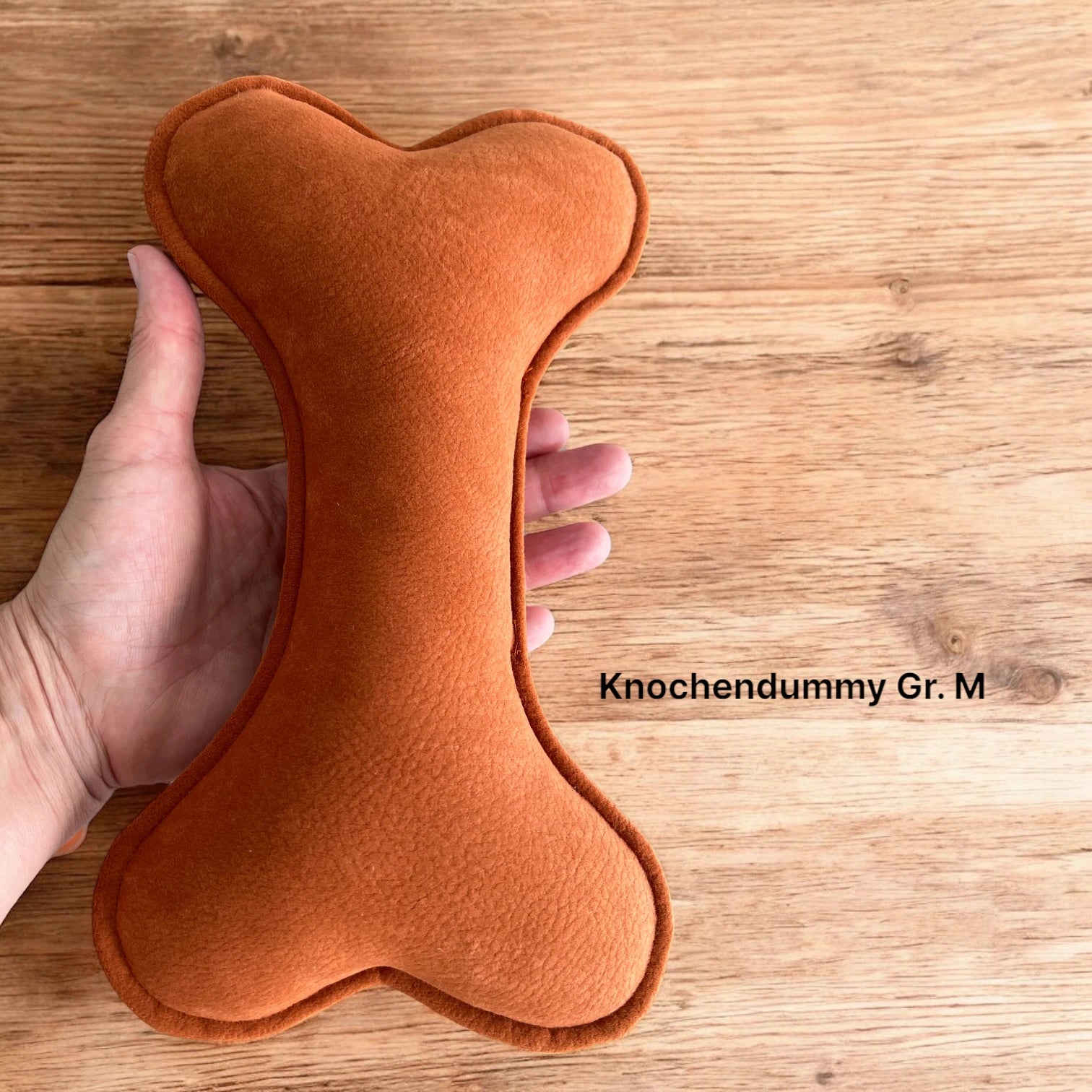 Knochendummy in marsrot und Größe M in der Hand liegend zum Größenvergleich