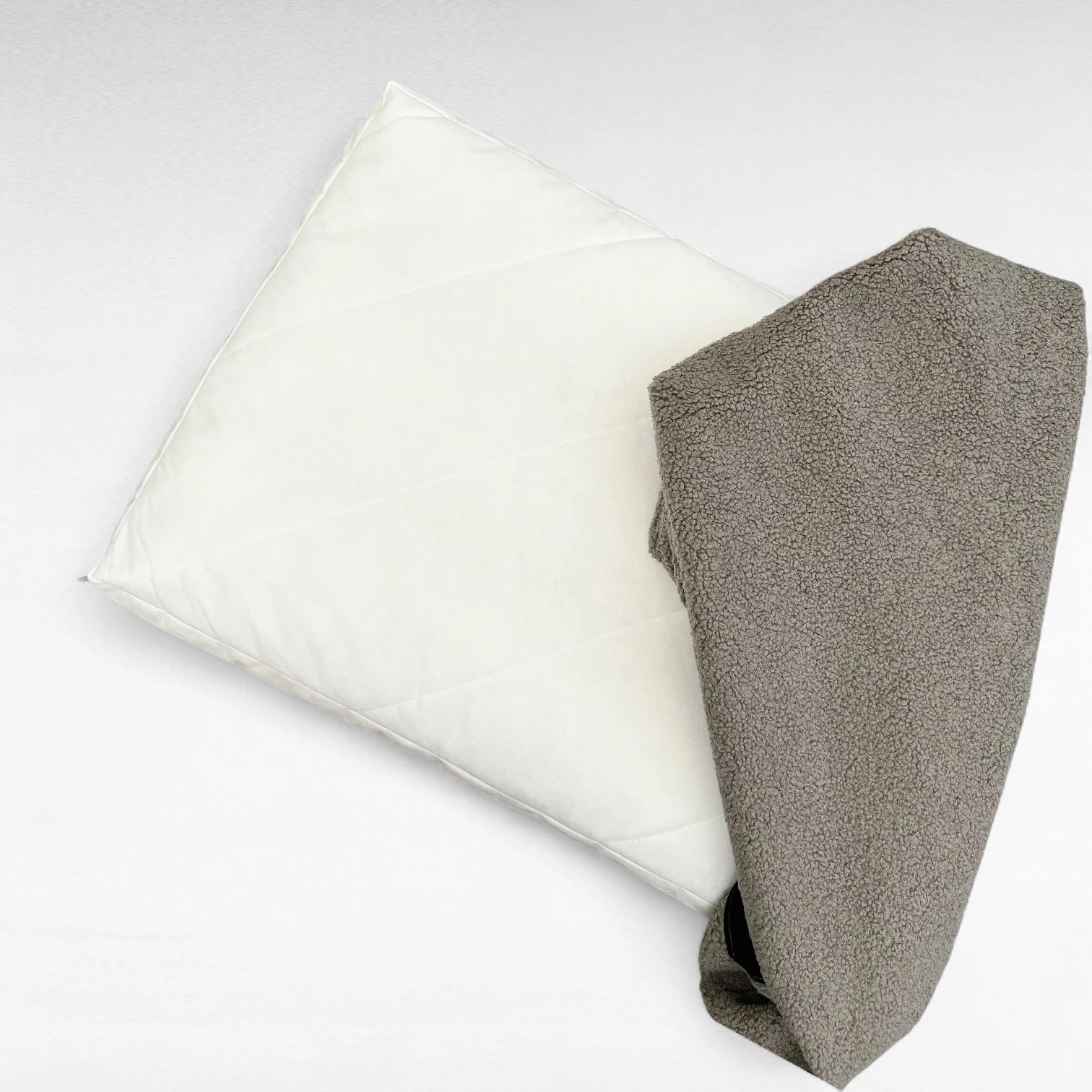 Rechteckige Hundematratze mit abnehmbarem grauem Bouclé-Bezug, teilweise auf weißem Innenkissen, vor hellem Hintergrund.