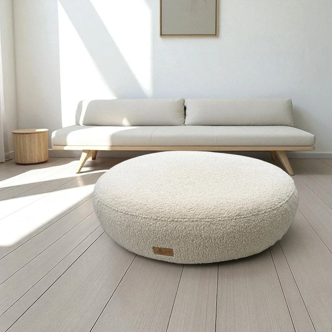 Rundes orthopädisches Hundebett mit kuscheligem Boucle Bezug auf Holzboden mit minimalistischer Couch im Hintergrund