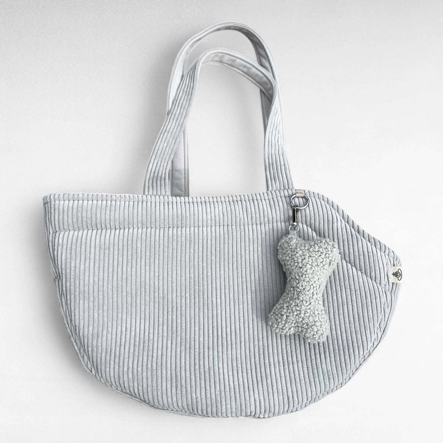 Halbrunde Hundetasche aus Cord hellgrau mit 2 Tragegurten aus Cordstoff, sowie silberner O-Ring und Taschenanhänger in Knochenform in Boucle hellgrau