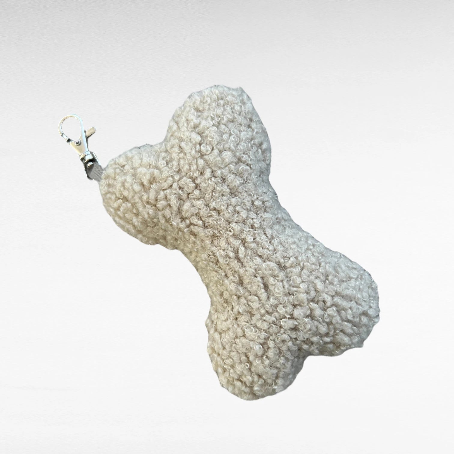 Knochenförmiges kleines Boucle-Kissen mit Karabinerhaken als Taschenanhänger in Farbe beige