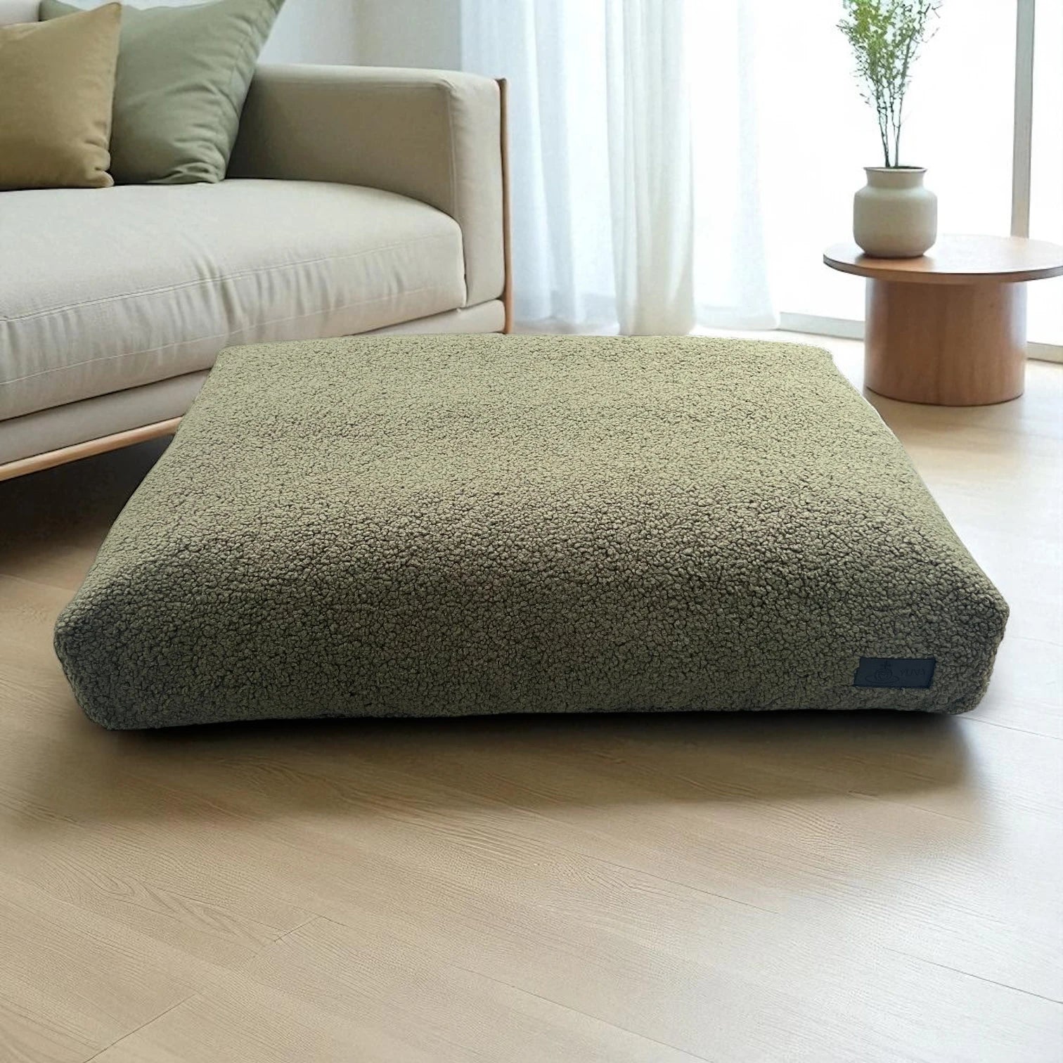Modernes, rechteckiges Hundekissen in Olivgrün aus weichem Bouclé-Stoff auf hellem Holzboden, neben einem hellen Sofa und Couchtisch im skandinavischen Wohnstil