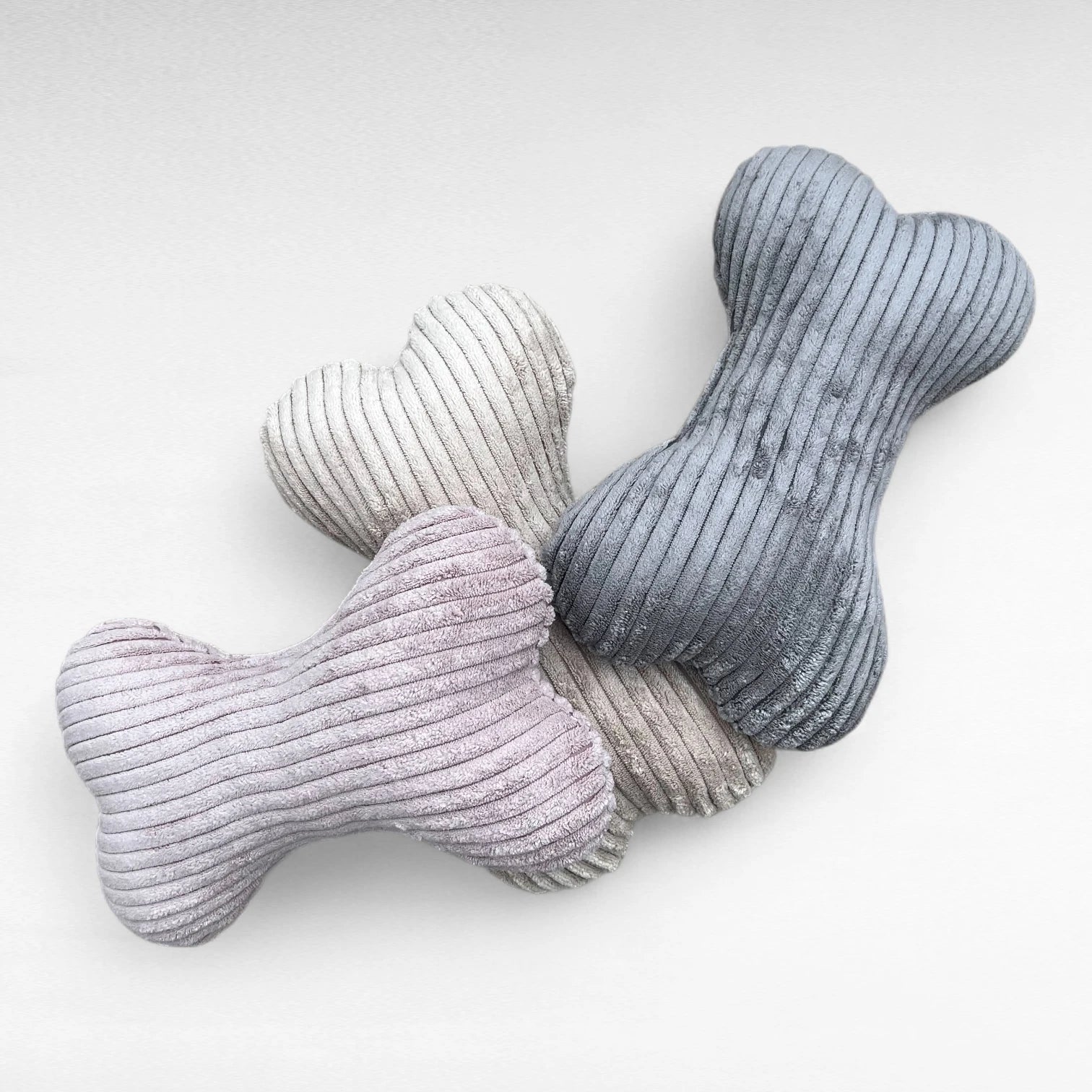 Drei Hundekissen in Knochenform aus Breitcord in den Farben beige, grau und pastellrosa übereinander gestapelt