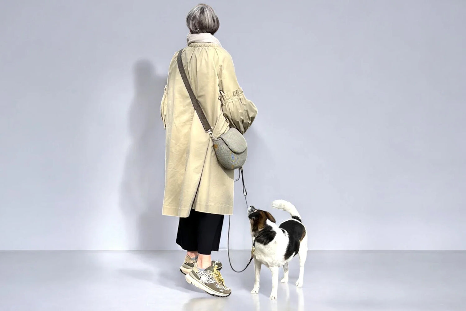 Frau stehend mit Hund an der Leine und eine Gassitasche in beige über der Schulter tragend