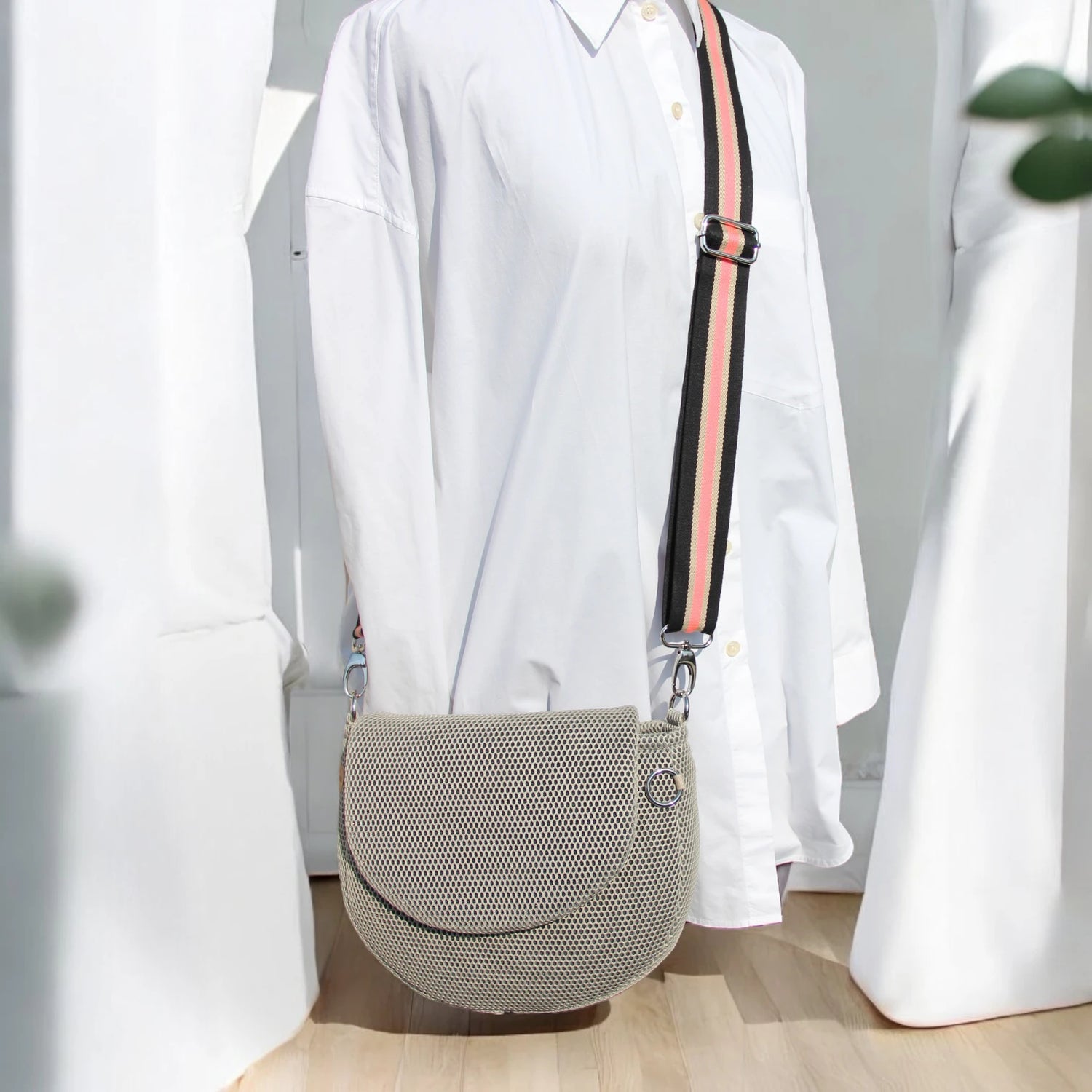 Halbrunde medium sized Gassitasche in Farbe beige aus Mesh Material mit beige_schwarz_koralle farbenen Tragegurt über Puppe hängend der Hintergrund ist minimalistisch