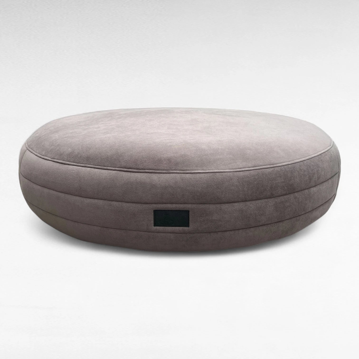 Taupefarbenes rundes Hundebett Yumi mit rundherum laufenden Steppungen uns schwarzem Yuna Label 
