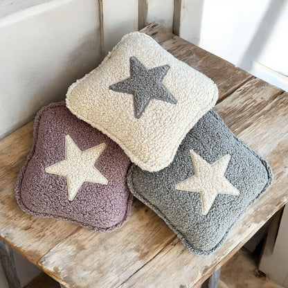 3 quadratische Kissen aus Boucle  in beige, altrosa und grau jeweils mit Stern Applikation auf Holztisch