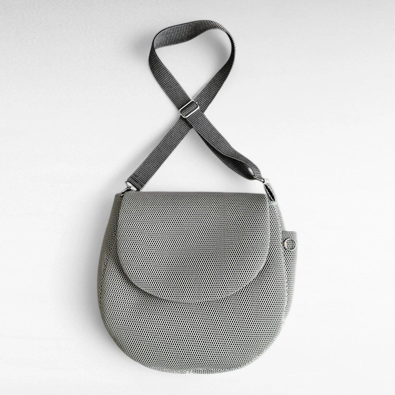 Runde oversized -Tasche mit Taschenklappe aus beigem Mesh Material mit beige-schwarzem Gurt und Metallelementen in silber