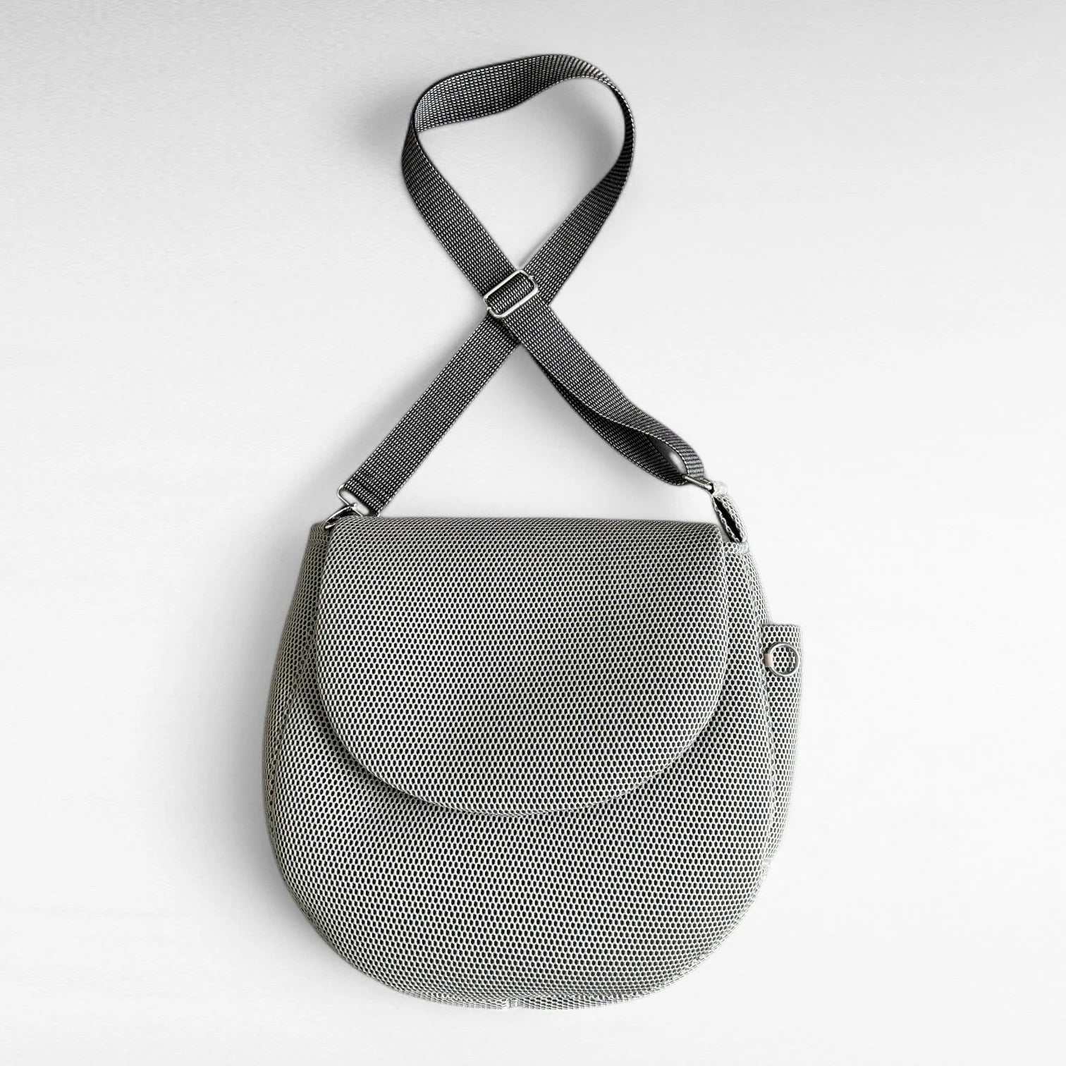 Runde oversized -Tasche mit Taschenklappe aus beigem Mesh Material mit beige-schwarzem Gurt und Metallelementen in silber
