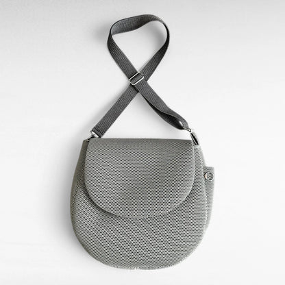 Runde oversized -Tasche mit Taschenklappe aus beigem Mesh Material mit beige-schwarzem Gurt und Metallelementen in silber