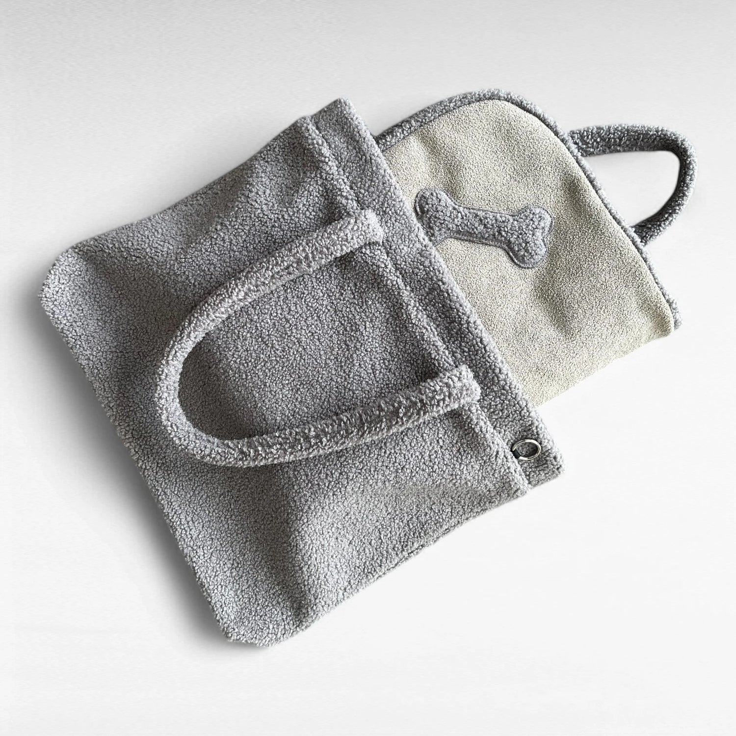 Grauer rechteckiger Teddyfellshopper mit schlammfarbener Hundedecke mit Knochenapplikation halb herausschauend