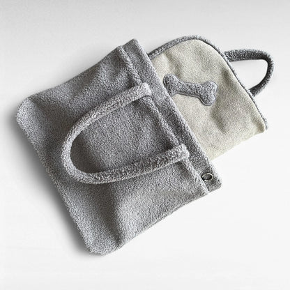 Grauer rechteckiger Teddyfellshopper mit schlammfarbener Hundedecke mit Knochenapplikation halb herausschauend