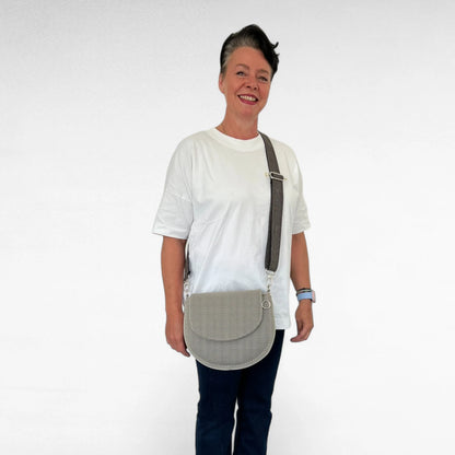 Frau in weiß dunkelblau gekleidet trägt halbrunde Gassitasche aus Mesh Material in beige mit beige melierten Tragegurt