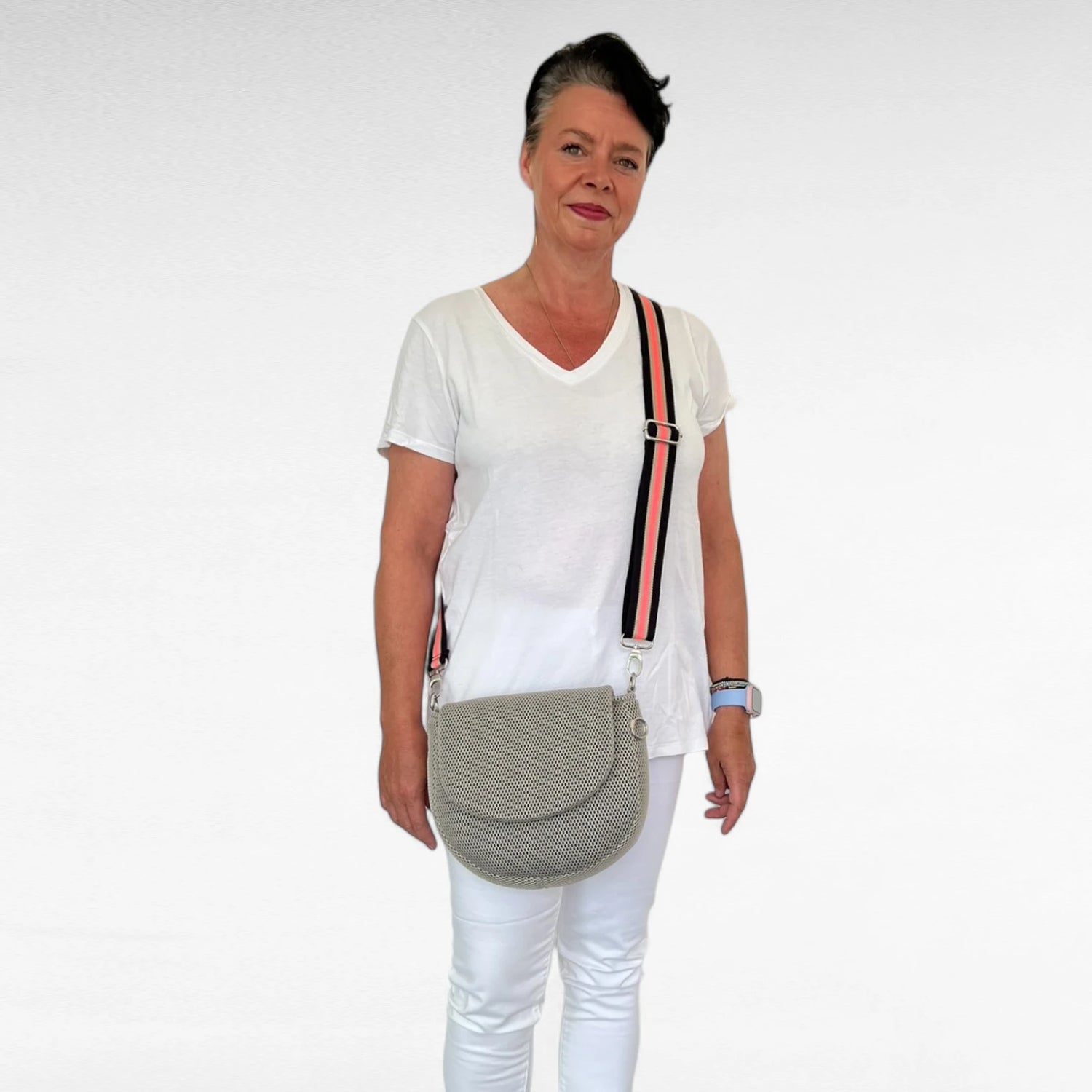 Frau in weiß gekleidet trägt halbrunde Gassitasche aus Mesh Material in beige mit schwarz korallefarbenen Tragegurt