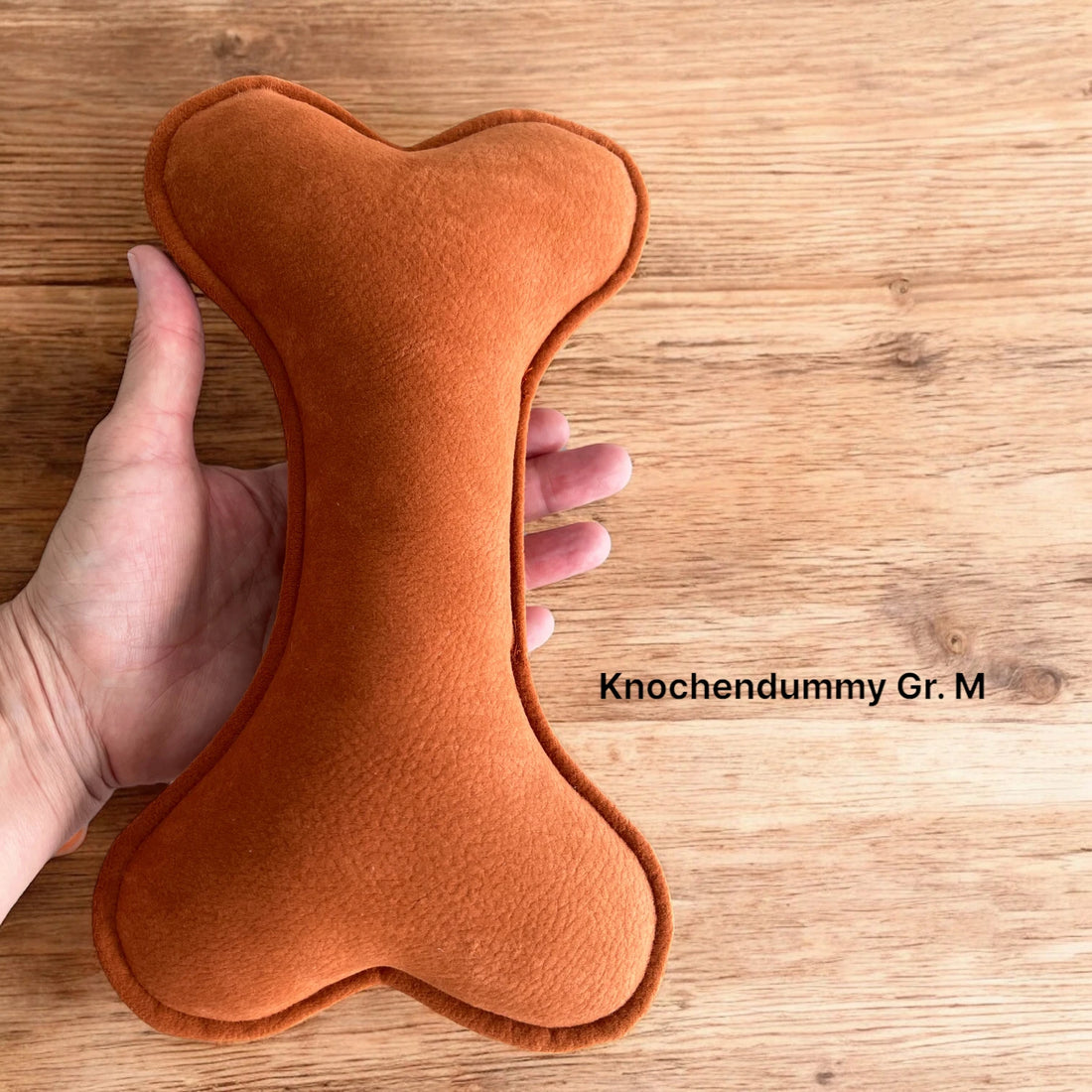 Knochendummy in marsrot und Größe M in der Hand liegend zum Größenvergleich
