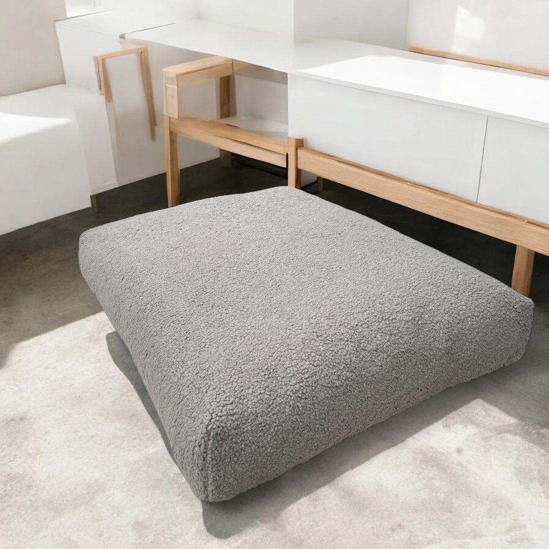Modernes Hundekissen in Grau aus weichem Bouclé-Stoff, platziert auf Betonboden in minimalistischem Raum mit Holz- und Weißmöbeln
