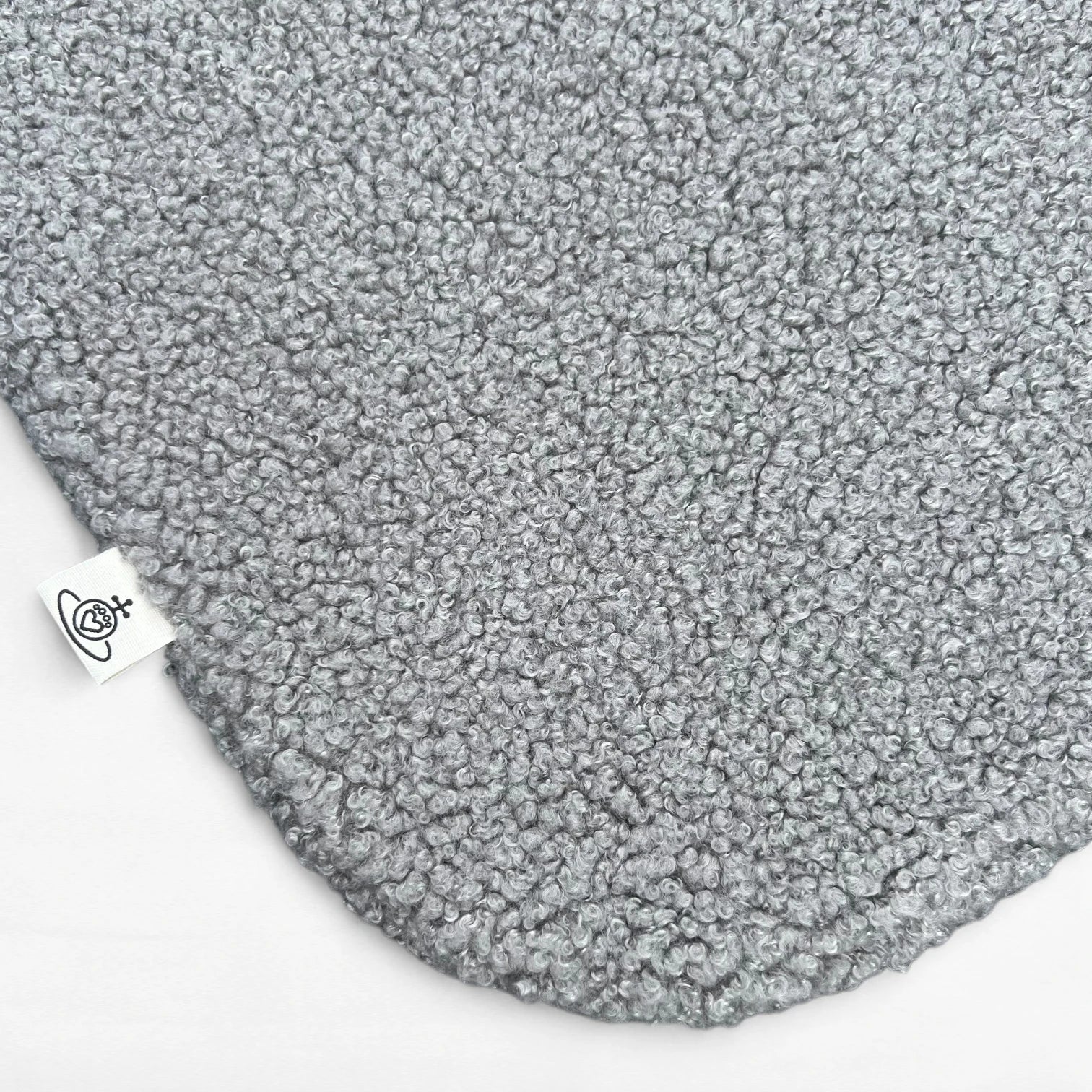 Nahaufnahme Hundedecke aus flauschigem Bouclé Stoff mit abgerundeten Kanten in grau und Logoetikett
