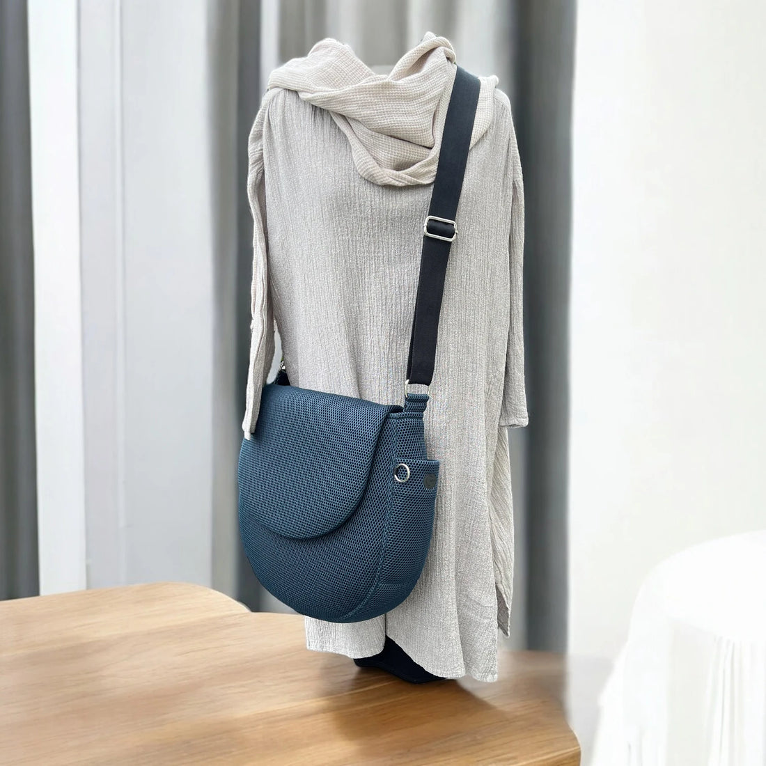 Blaue oversized Crossbody Tasche aus Mesh Material mit schwarzem Gurt über Mannequinpuppe präsentiert