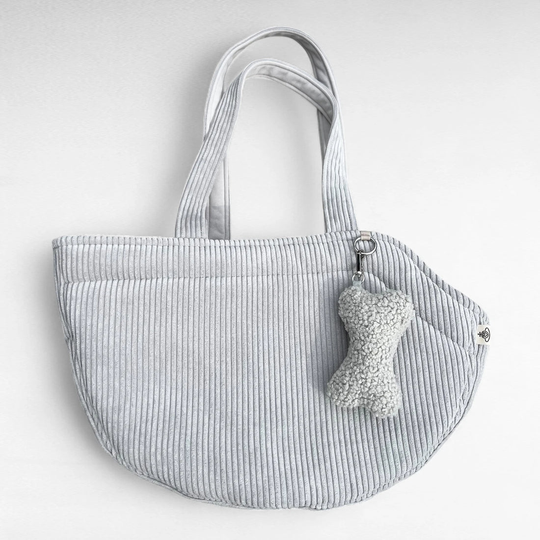 Halbrunde Hundetasche aus Cord hellgrau mit 2 Tragegurten aus Cordstoff, sowie silberner O-Ring und Taschenanhänger in Knochenform in Boucle hellgrau